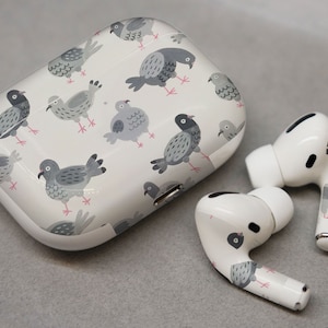 May include: White wireless earbuds with a charging case. The case has a white background with a repeating pattern of gray pigeons.