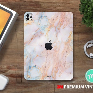 May include: A white, blue and gold marble phone case with a camera cutout and the Apple logo. The case is made of 3M premium vinyl.