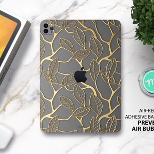 Könnte beinhalten: Eine graue iPad-Hülle mit einem goldenen Blatt-Muster. Die Hülle hat eine luftfreisetzende Kleberückseite, die Luftblasen verhindert.
