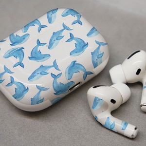 May include: White wireless earbuds with a blue whale pattern on the case and earbuds. The case is open and the earbuds are sitting next to it.