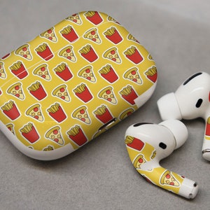 Könnte beinhalten: Weiße kabellose Ohrhörer und Ladecase mit gelbem Hintergrund und einem sich wiederholenden Muster aus Pizzastücken und roten Pommes-Behältern. Die Ohrhörer befinden sich neben dem Ladecase.