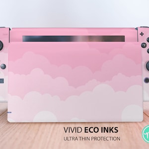Puede incluir: Piel de consola Nintendo Switch rosa y blanca con un diseño de nubes. La piel es ultra fina y está hecha con tintas ecológicas. La piel se muestra sobre una superficie de madera.