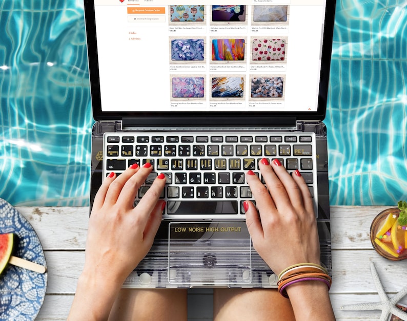 May include: A laptop computer with a custom keyboard cover featuring a cassette tape design. The laptop is open and the screen shows a website with images of different laptop skins. The text "LOW NOISE HIGH OUTPUT" is visible on the keyboard cover.
