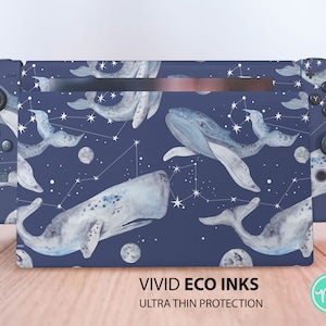 Könnte beinhalten: Eine blaue Nintendo Switch Konsolenhaut mit einem Aquarelldesign von Walen und Sternen. Die Haut verfügt über ein Sternbildmuster und den Text "VIVID ECO INKS ULTRA THIN PROTECTION".