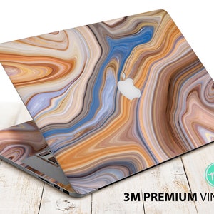 May include: A laptop computer with a colourful abstract marble design skin. The skin is made of 3M premium vinyl. The laptop is closed and sitting on a wooden surface.