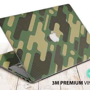 Puede incluir: Un ordenador portátil con una piel de vinilo de camuflaje verde, marrón y beige. La piel tiene un diseño geométrico con formas redondeadas. El portátil está abierto y la pantalla está orientada hacia atrás. El portátil está sobre una superficie de madera. El texto "3M PREMIUM VINYL" está impreso en la superficie debajo del portátil.