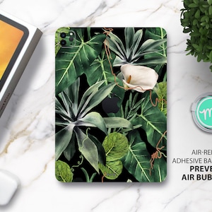 Può includere: Una custodia per telefono nera con un design a foglie tropicali. La custodia presenta grandi foglie verdi e un fiore bianco con uno stelo marrone. Il testo "AIR-RELEASE ADHESIVE BACKING PREVENTS AIR BUBBLES" è stampato nella parte inferiore dell'immagine.