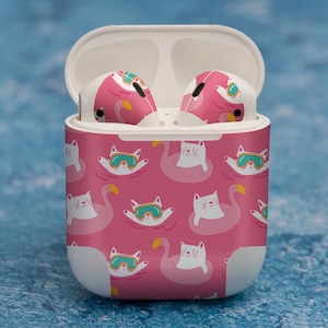 May include: White wireless earbuds case with a pink and white design featuring cats wearing sunglasses and floating on pink flamingos.