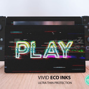 Könnte beinhalten: Eine schwarze Nintendo Switch Konsole mit einer benutzerdefinierten Haut, die eine glitchige, farbenfrohe "PLAY" Grafik zeigt. Die Haut wird als "VIVID ECO INKS ULTRA THIN PROTECTION" beschrieben.