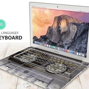 May include: A silver laptop computer with a black and gold keyboard cover. The keyboard cover has a design that looks like a vintage record player. The laptop screen shows a picture of a mountain range.