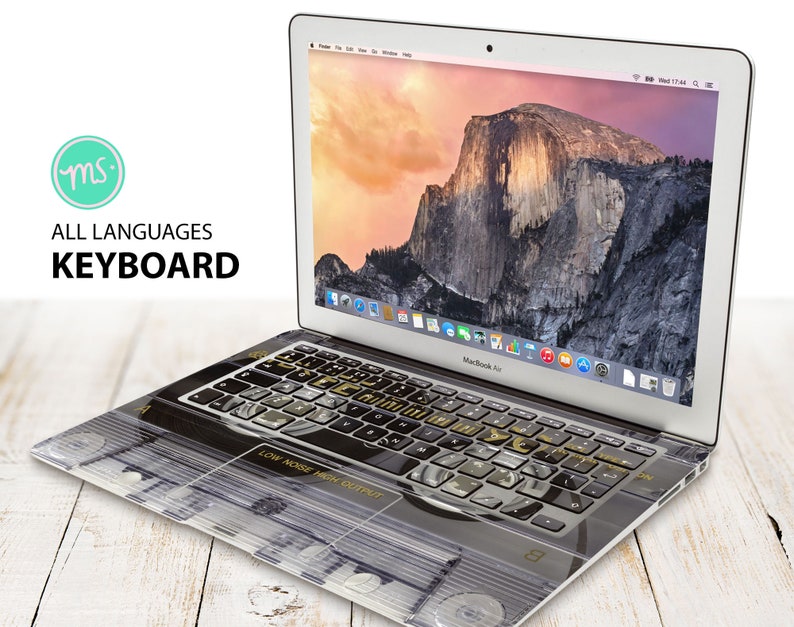 May include: A silver laptop computer with a black and gold keyboard cover. The keyboard cover has a design that looks like a vintage record player. The laptop screen shows a picture of a mountain range.