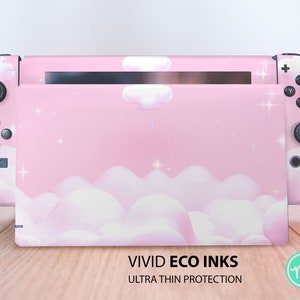 Könnte beinhalten: Rosa Nintendo Switch Konsole mit einer benutzerdefinierten Haut mit einem rosa und weißen Wolkenmuster mit funkelnden Sternen. Die Haut ist mit "VIVID ECO INKS ULTRA THIN PROTECTION" beschriftet.