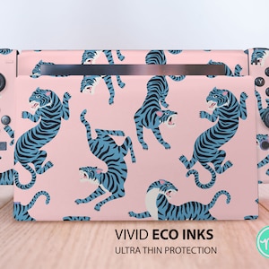 Può includere: Una skin per console Nintendo Switch rosa con un motivo a tigre blu e bianco. La skin ha il testo "VIVID ECO INKS ULTRA THIN PROTECTION" stampato in basso.