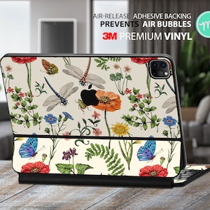 Puede incluir: Una funda blanca para iPad con un patrón floral que incluye mariposas y libélulas. La funda tiene un borde negro y un logotipo de 3M. El texto "Air-Release Adhesive Backing Prevents Air Bubbles 3M Premium Vinyl" está impreso en la funda.