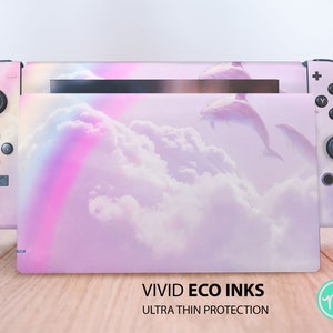 May include: A pink and white Nintendo Switch console skin with a pastel rainbow and clouds design. The skin features dolphins jumping in the clouds. The text "VIVID ECO INKS ULTRA THIN PROTECTION" is printed on the bottom of the skin.