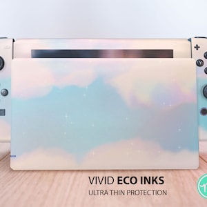 Puede incluir: Una piel para consola Nintendo Switch de color azul claro y rosa con un diseño nublado y un borde blanco. La piel está etiquetada con "VIVID ECO INKS ULTRA THIN PROTECTION".