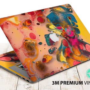 Puede incluir: Un ordenador portátil con un diseño abstracto colorido en la tapa. El diseño presenta una mezcla de colores amarillos, naranjas, rojos, azules y verdes en un patrón de remolino. El portátil está abierto y la pantalla es visible. El portátil está sentado en una superficie de madera. 3M Premium Vinyl.