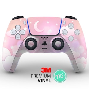 Puede incluir: Un mando de PlayStation 5 rosa y blanco con un diseño de nubes y estrellas. El mando tiene el logotipo de 3M y el texto "PREMIUM VINYL".