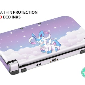 Può includere: Una console Nintendo 3DS XL bianca con una skin personalizzata che presenta un personaggio Pokémon blu e bianco su uno sfondo nuvoloso viola e bianco con stelle. Il testo "ULTRA THIN PROTECTION" e "VIVID ECO INKS" è stampato sulla parte superiore della console.