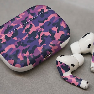 May include: A white wireless charging case for AirPods with a pink and purple camouflage pattern. The case is closed and the two AirPods are shown next to it.