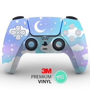 Puede incluir: Un mando de PlayStation 5 azul y morado con un diseño de luna y estrellas. El mando tiene el logotipo de 3M y el texto "PREMIUM VINYL" en la parte inferior.