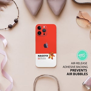 May include: A red phone case with a white border and a cartoon character on it. The case has the text "NAGOYA" and "PANTONE P 45-8 C" on it. The case is designed to prevent air bubbles when applied to a phone.