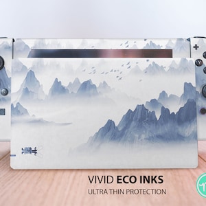 May include: A white Nintendo Switch console with a custom skin featuring a blue and white watercolor mountain landscape. The text "VIVID ECO INKS ULTRA THIN PROTECTION" is printed on the bottom of the console.