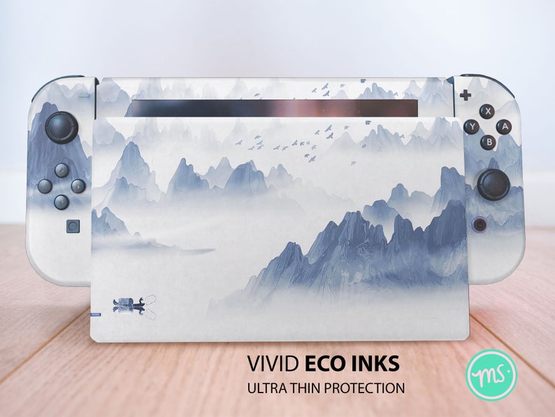 May include: A white Nintendo Switch console with a custom skin featuring a blue and white watercolor mountain landscape. The text "VIVID ECO INKS ULTRA THIN PROTECTION" is printed on the bottom of the console.