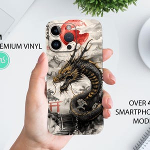 May include: A black and gold dragon design phone case with a red and white sun graphic. The case is for an iPhone with a camera lens cutout. The case has a 3M premium vinyl sticker.