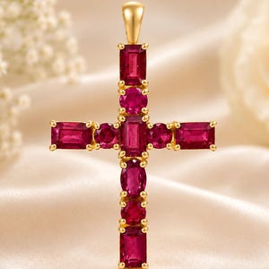 Puede incluir: Un colgante de cruz en oro con una disposición vertical de tres rubíes de corte rectangular y dos de corte ovalado, con una barra horizontal que contiene dos rubíes rectangulares y dos redondos, engastados en un marco de oro amarillo pulido.