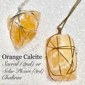 May include: Two orange calcite crystal necklaces, one with a silver chain and one with a gold chain. The crystals are wrapped in wire and are said to be associated with the sacral or solar plexus chakras.