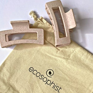 Peut inclure: Deux pinces à cheveux roses en plastique moucheté dans un sac en toile beige avec le logo "ecosophist" imprimé dessus.