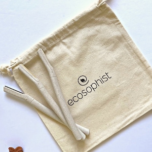 May include: Three beige razors are displayed on a beige drawstring bag. The bag has the word "ecosophist" printed on it in black. The razors are made of a light-colored material and have a textured appearance. The bag is made of a natural-colored fabric.