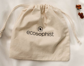 May include: A beige drawstring bag with the word "ecosophist" printed in black. The bag is made of a natural-colored fabric and has a simple, minimalist design. The bag is closed with a drawstring.