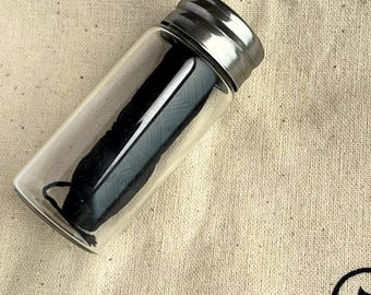 May include: A glass jar with a silver lid containing black dental floss.