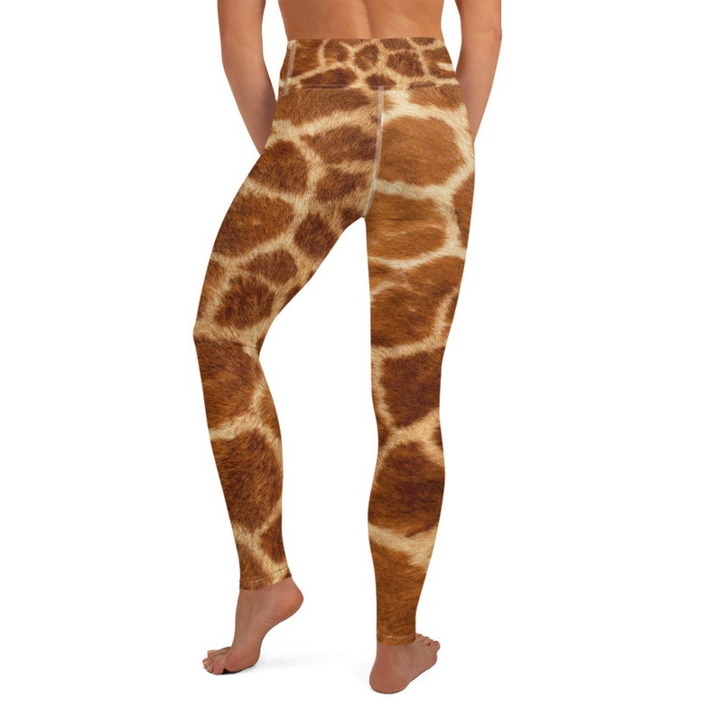May include: Brown and tan giraffe print leggings. The leggings feature a high waist and a realistic giraffe pattern. The fabric appears to be soft and stretchy, suitable for yoga or other activities. The leggings are shown from the back.