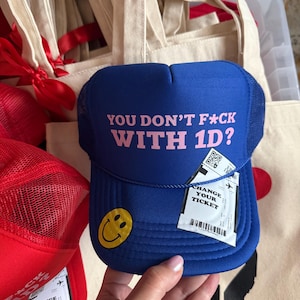 May include: Blue and black mesh trucker hat with a yellow smiley face and the text "YOU DON'T F*CK WITH 1D?" in pink letters.