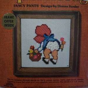May include: Needlepoint kit featuring a girl in a red dress and blue overalls holding a basket of flowers. The kit includes 100% cotton canvas, 100% wool yarn, a needle, mounting board, and instructions. It fits a standard 5x5 inch frame. The kit is called "Fancy Pants" and is designed by Donna Kooler.