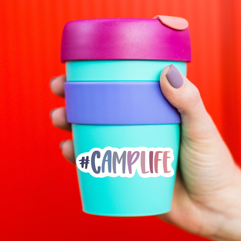 May include: A reusable turquoise blue travel mug with a purple, blue, and pink lid. The mug has a white sticker with the text "#CAMPLIFE" in a rainbow gradient.