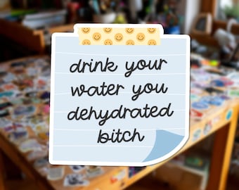Può includere: Un adesivo quadrato con sfondo azzurro e linee orizzontali bianche. In alto, una striscia gialla presenta un motivo ripetuto di faccine sorridenti nere. Il testo recita: drink your water you dehydrated bitch in corsivo grigio scuro.