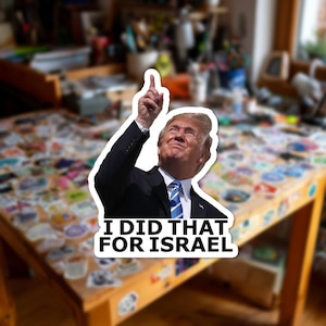 May include: A sticker featuring a portrait of a man in a suit pointing upwards. The text "I DID THAT FOR ISRAEL" is printed in bold white letters below the portrait. The sticker is likely for political or novelty purposes.