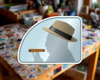 Può includere: Un adesivo grafico raffigurante un cappello fedora marrone chiaro con una fascia nera e un sigaro marrone. Il design mostra la sagoma di una testa di profilo su uno sfondo azzurro, racchiusa in una cornice arrotondata con bordo bianco.