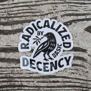 May include: A white sticker featuring black text and a black bird illustration. The sticker says "RADICALIZED BY BASIC DECENCY" in a circular design. The bird is holding a sprig in its beak.