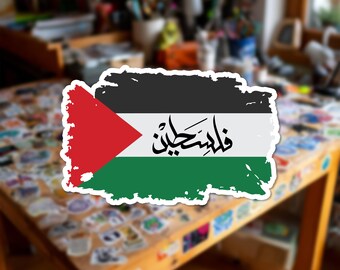 Può includere: Un adesivo rettangolare raffigurante la bandiera della Palestina con un bordo dall'effetto pennellata. Il design include una striscia superiore nera, una striscia centrale bianca con calligrafia araba nera, una striscia inferiore verde e un triangolo rosso.