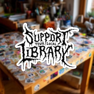 Puede incluir: Una pegatina troquelada con el texto "SUPPORT YOUR LOCAL LIBRARY" en una fuente negra, dentada y de estilo heavy metal. Las letras tienen un aspecto goteante y ramificado con bordes afilados y puntiagudos, sobre un borde de fondo blanco.