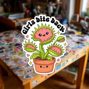 Puede incluir: Una pegatina troquelada que muestra una planta carnívora Venus atrapamoscas de dibujos animados en una maceta de terracota con cara sonriente. La planta tiene hojas verdes con interior rosa y bordes espinosos. El texto Girls bite back aparece arriba.