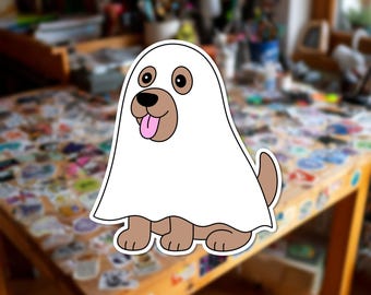 Può includere: Un adesivo a cartone animato di un cane marrone che indossa un costume da fantasma bianco. Il cane ha occhi grandi, un naso nero e una lingua rosa che sporge. Il design presenta un bordo bianco spesso attorno ai contorni dell'immagine.
