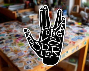 Può includere: Un adesivo nero fustellato a forma di mano che esegue il saluto vulcaniano. Il testo bianco integrato nel design recita "LIVE LONG & PROSPER" con un carattere audace e stilizzato. L'adesivo presenta un netto bordo bianco di contorno.