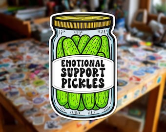 Può includere: Un adesivo fustellato raffigurante un barattolo di vetro in stile cartoon pieno di cetriolini verde brillante. Il barattolo ha un coperchio giallo e un'etichetta bianca con il testo nero "EMOTIONAL SUPPORT PICKLES" in un font retrò ondulato.