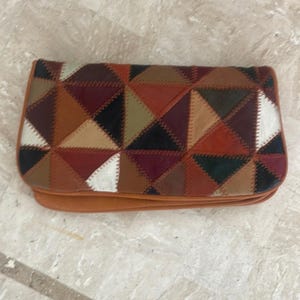 May include: A brown leather clutch purse with a patchwork design of various colors and shapes. The purse is made of different pieces of leather sewn together to create a geometric pattern.